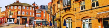 Orange-brick buildings and a street scene with shopfronts, signs, and closed blue parasols.