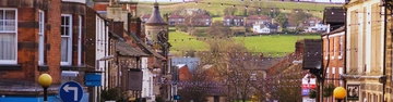 View down a town street towards green fields and houses in the distance.