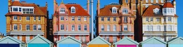 Colourful beach huts in front of pastel town houses.
