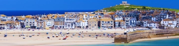 Sandy beach with boats and seaside houses on a hillside by the sea.