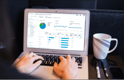 A person reviewing an analytics dashboard on a laptop beside a mug and notebook.