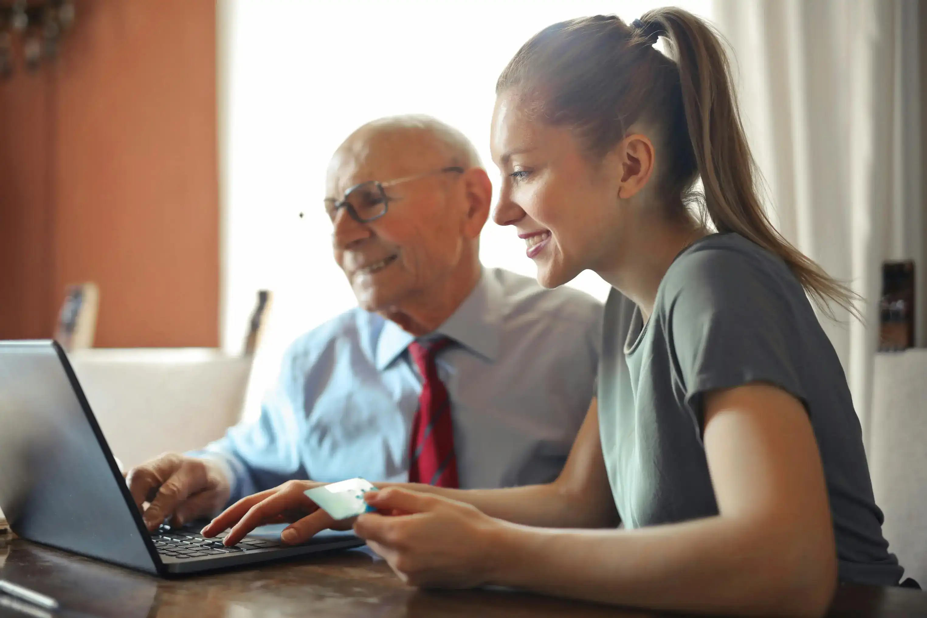 An older man and younger woman smiling while using a laptop.