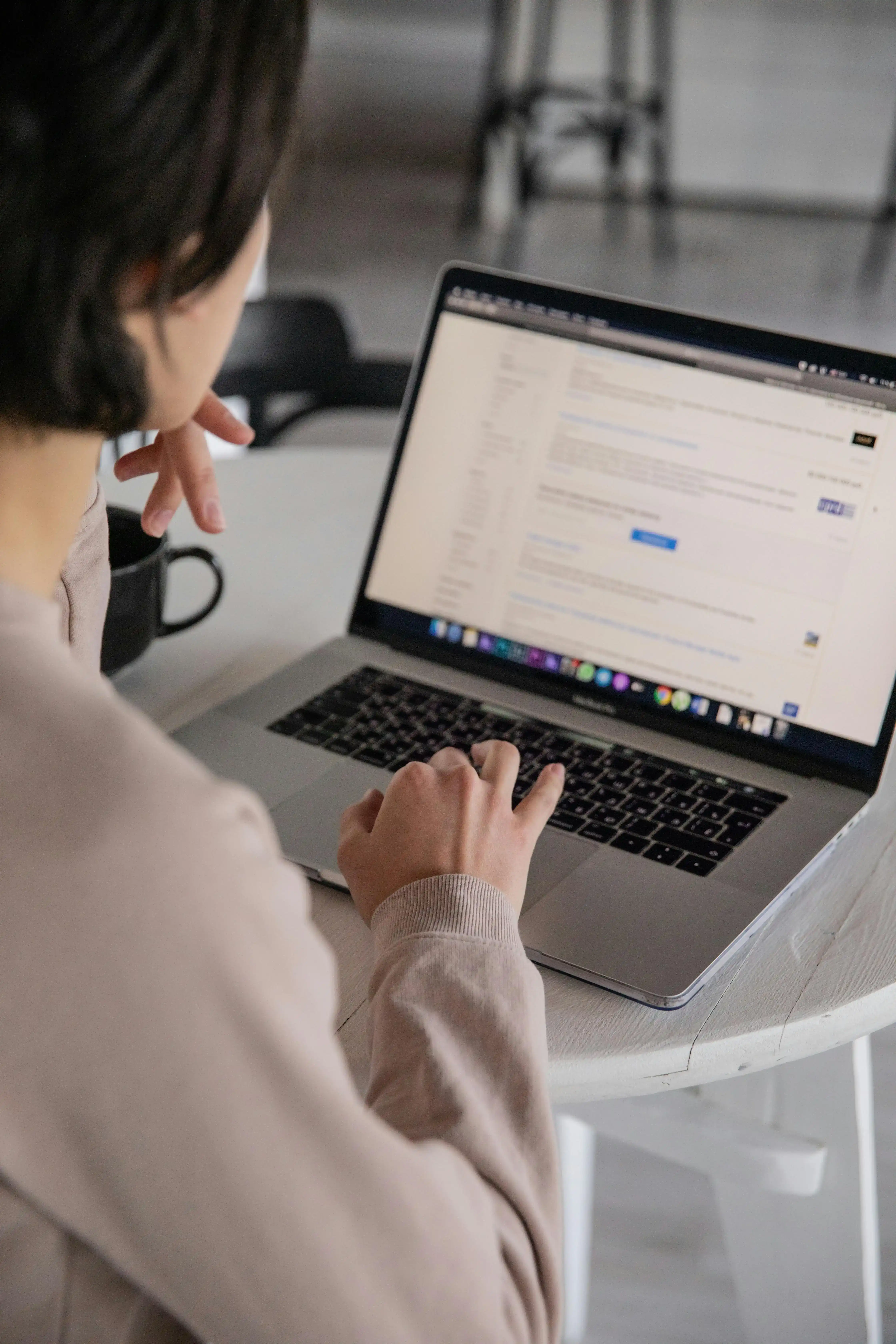 Person working on a laptop at a desk with a mug nearby.