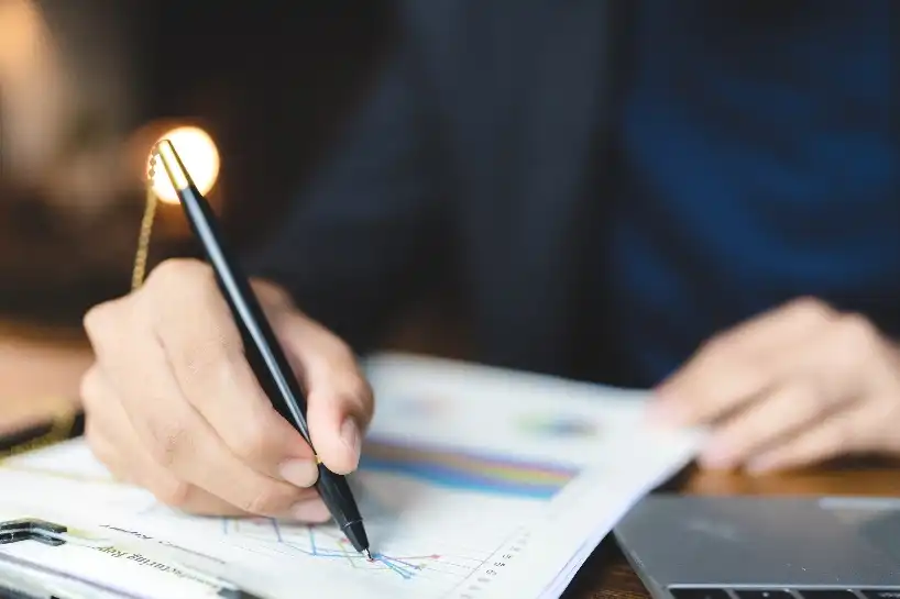 Hand marking a printed chart beside a laptop.